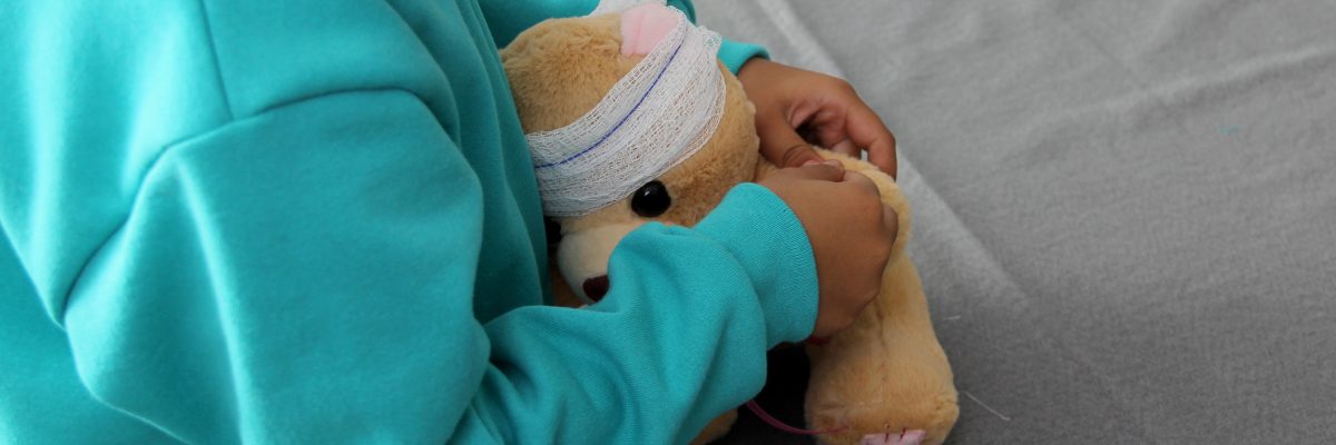 4-year-old brunette Latina girl with glasses represents mistreatment and physical abuse in her teddy bear with bandages on her head